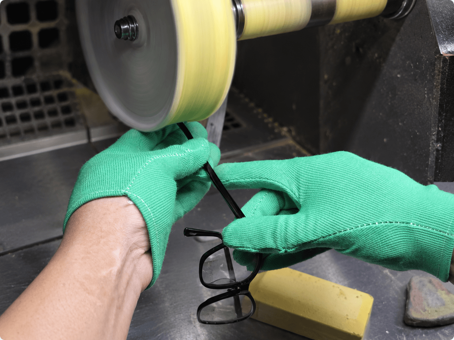 Worker polishing an optical frame at a rotating buffing wheel