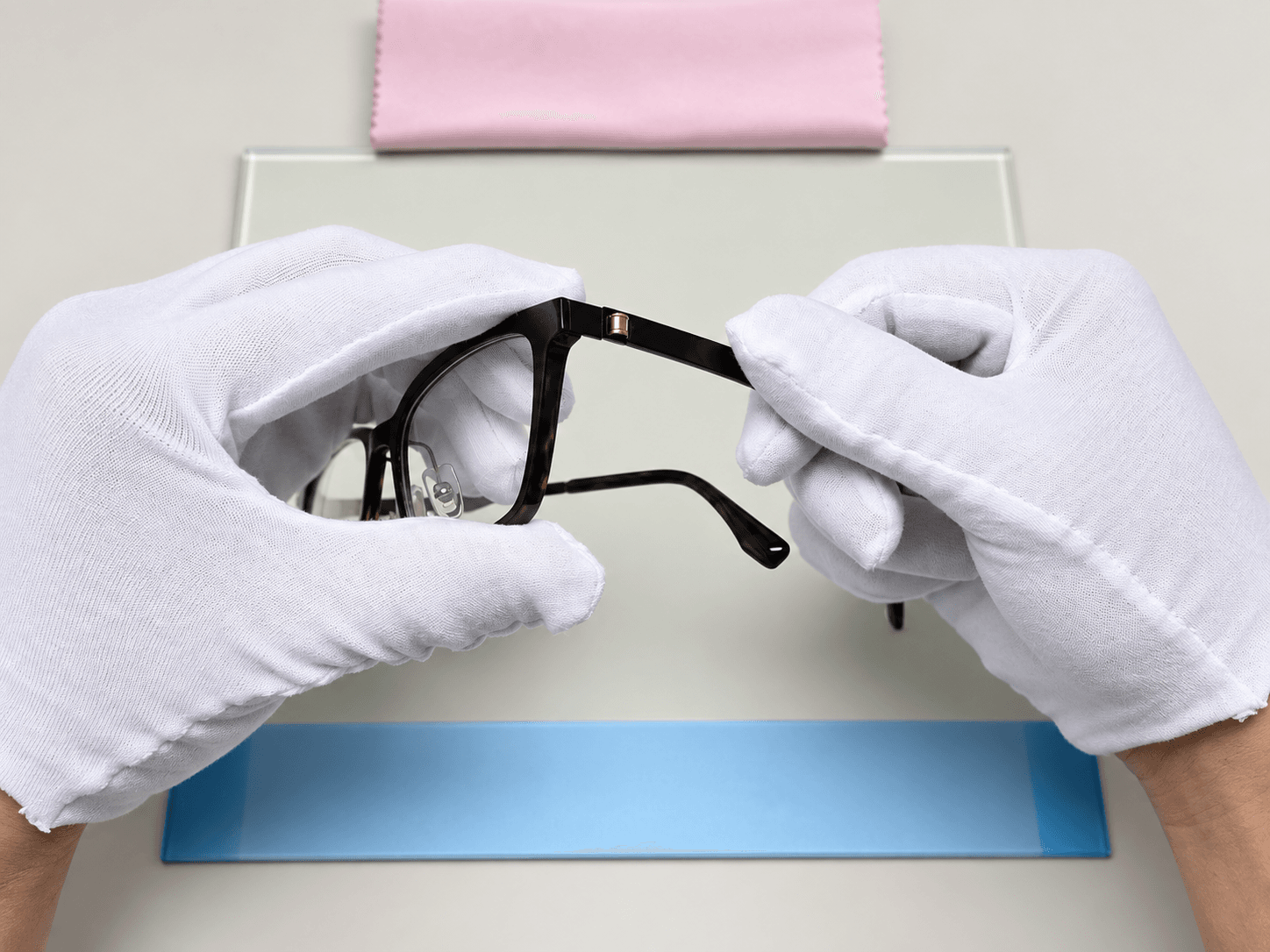 Gloved hands checking an optical frame at an inspection station