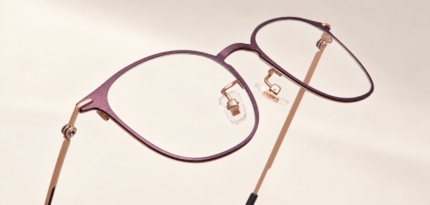 Angled close-up of the plum titanium frame front with rose-gold-tone detailing and clear lenses.