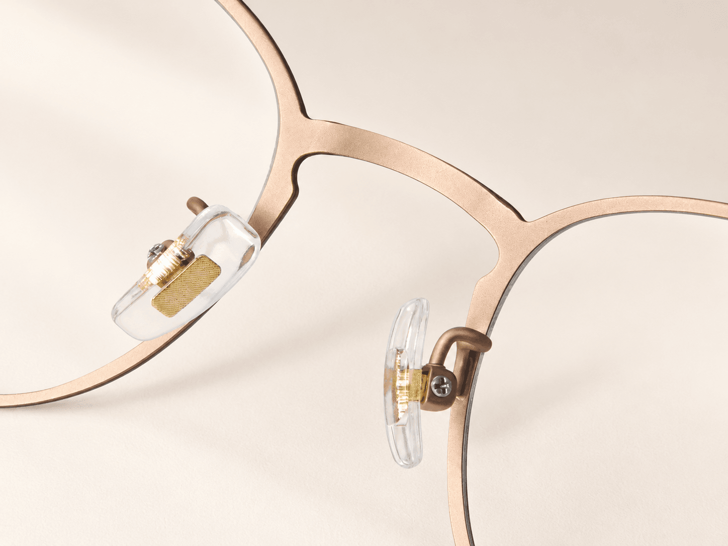 Reverse bridge close-up with clear nose pads, gold-tone inserts and curved metal supports.