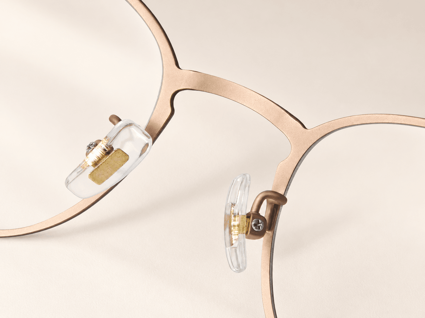 Reverse bridge close-up with clear nose pads, gold-tone inserts and curved metal supports.